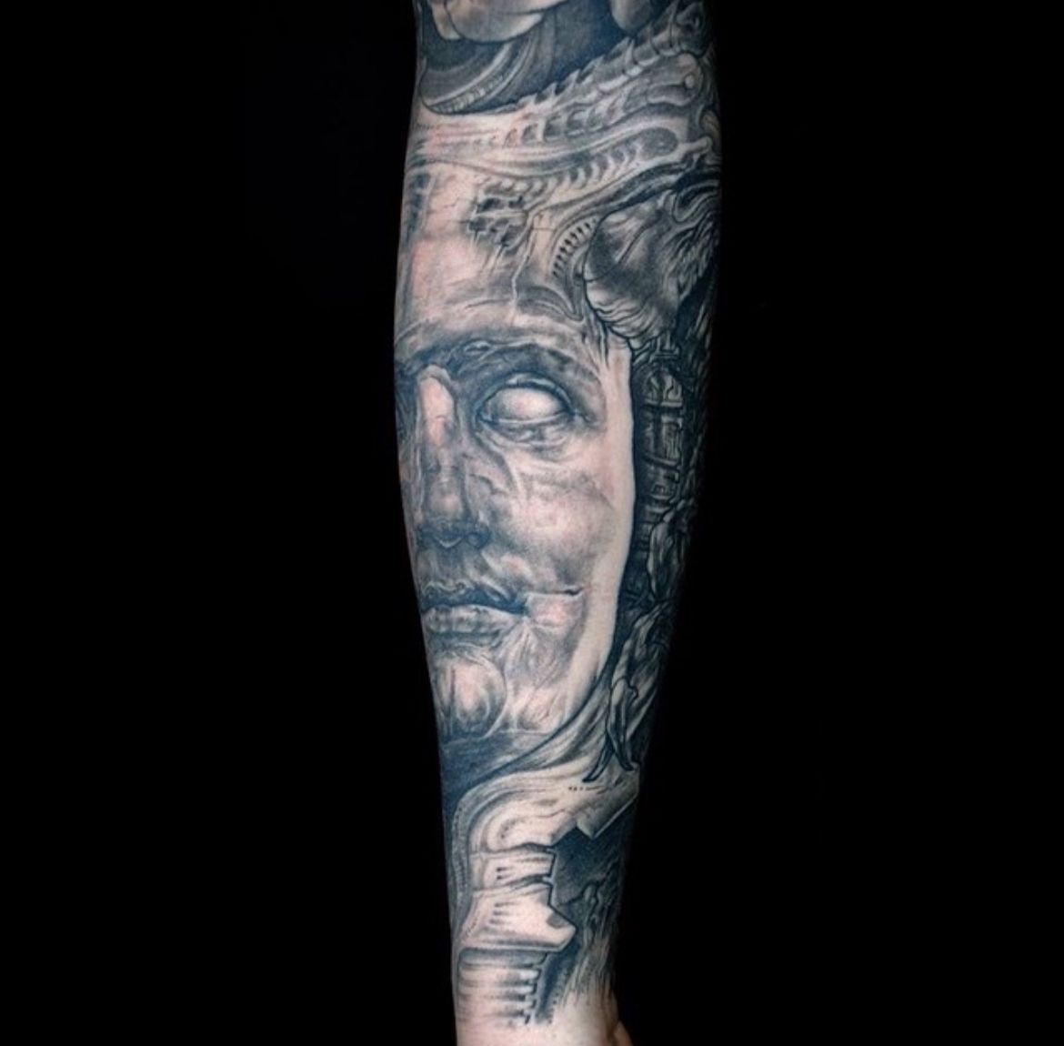 Biomechanic tatuering i svart och grått som följer armens muskler och struktur.