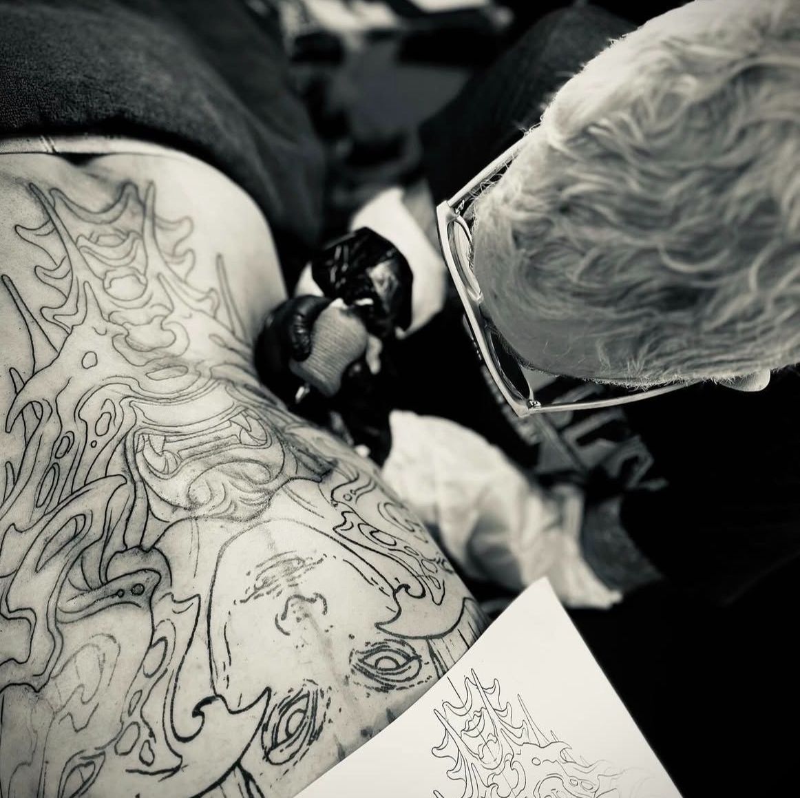 Tatuerare applicerar första linjearbetet på överarm.